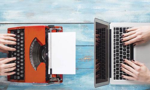 an old red typewriter across from a sleek new Mac laptop