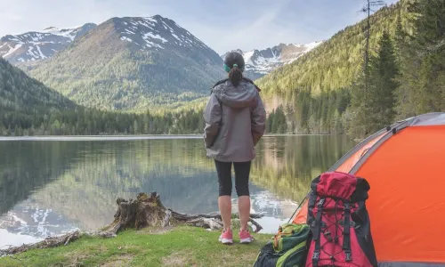 Woman at campsite looks over a lake to a distant mountain peak