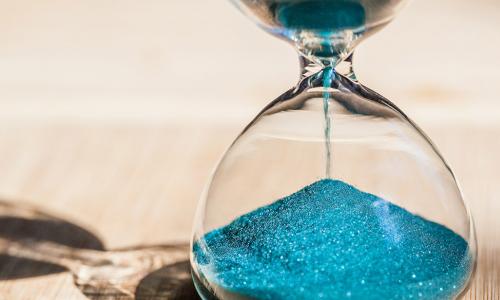 Blue sand running through the bulbs of an hourglass measuring the passing time in a countdown to a deadline