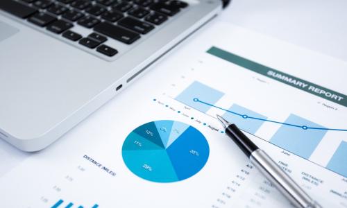 laptop and pen next to financial investment report charts