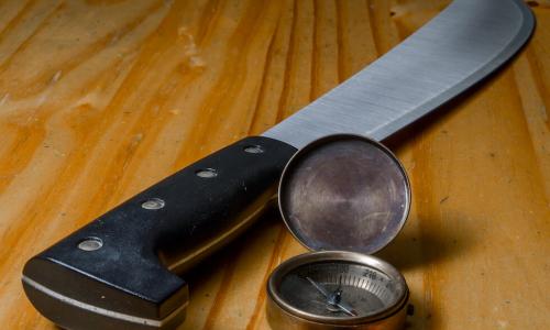 Machete and compass in wood background