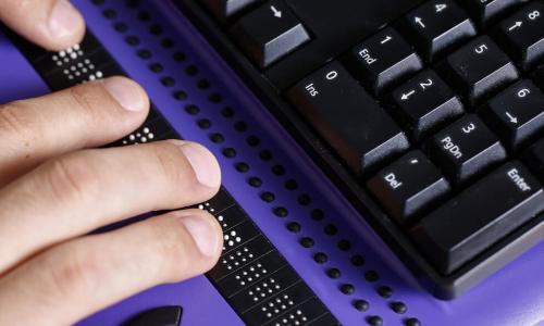 Blind person using computer with braille computer display and a computer keyboard