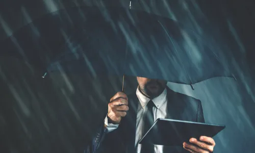 business man holds tablet under an umbrella on a dark rainy day