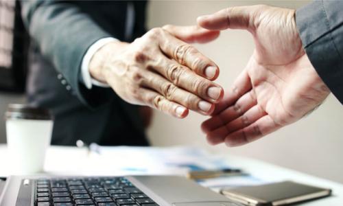 business men shake hands over computer