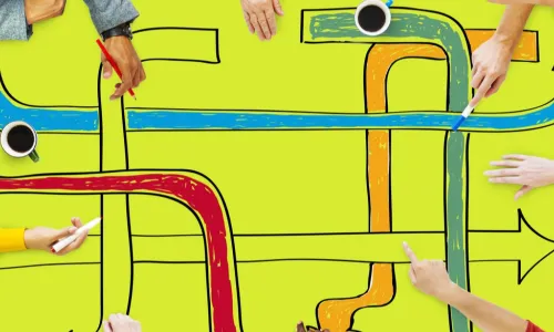 people at a table drawing a maze of arrow pathways with markers