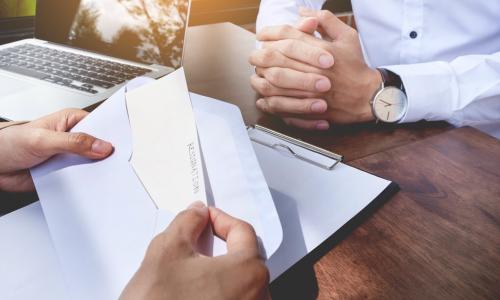 Manager reading a resignation letter across the table from employee