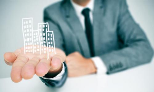 a businessman sitting in a desk showing a pile of drawn buildings in his hand