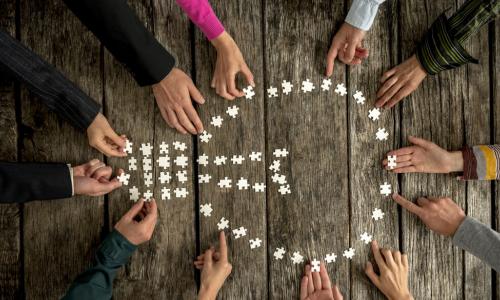 hands create a lightbulb with puzzle pieces on a wooden table