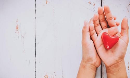 hands holding a red heart over a white wooden background