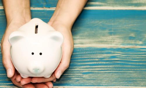 hands holding white piggy bank on a blue wood table