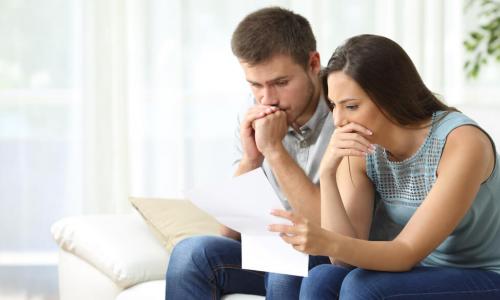Worried couple reading an important notification in a letter sitting on a couch in the living room at home
