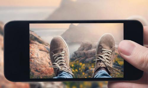 person looking through smartphone camera at their shoes and mountain vista beyond