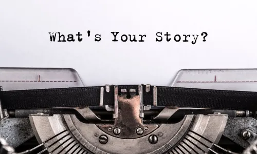 The text What’s Your Story typed on paper above a typewriter
