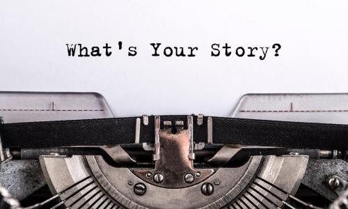 The text What’s Your Story typed on paper above a typewriter