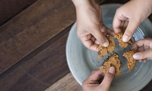 multiple hands reaching toward plate to take pieces of a cookie