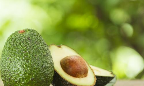 whole unripe avocado next to a ripe avocado sliced in half with pit showing