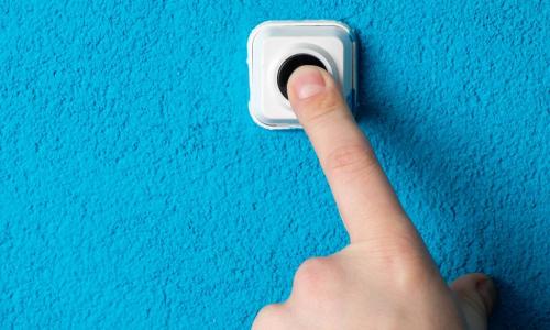 finger pressing doorbell on a blue wall