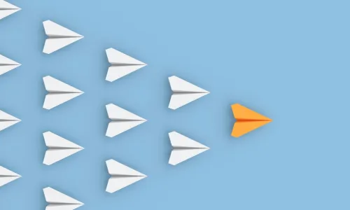 orange paper airplane leading a group of white paper airplanes in formation