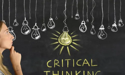 woman standing before chalkboard thinking about the drawing of a set of light bulbs, one of them in yellow as if lit up