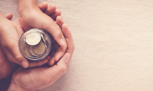 adult hands holding child's hands around a savings jar