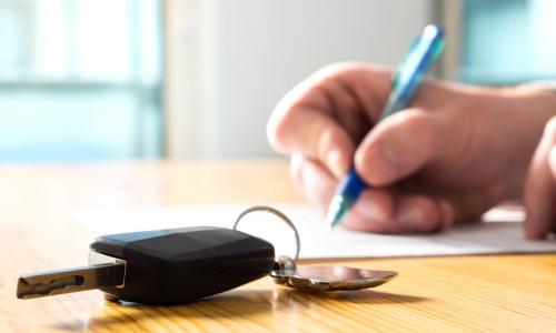 member signing contract for auto loan with car keys laying on table