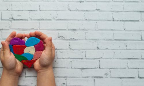 child’s hand holding multi-color, patchwork clay heart