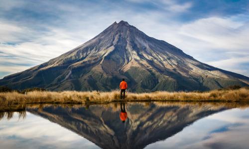 mountaineer looking at mountain with reflection of mountain behind in lake