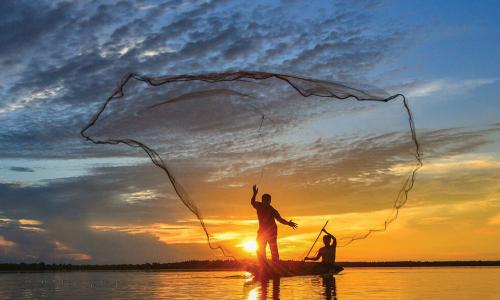 two fishermen in rowboat casting a wide net into water