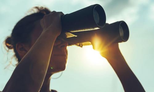 woman looking through binoculars against sunny blue sky