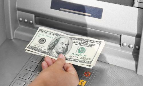 hand withdrawing $100 bills from ATM