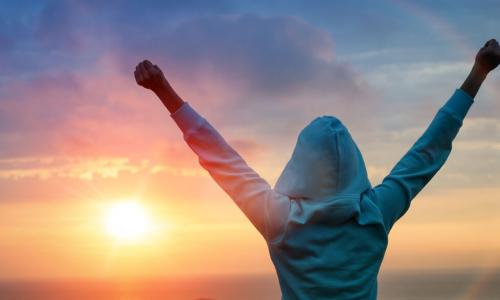 a woman at sunrise at the beach raises arms in victory