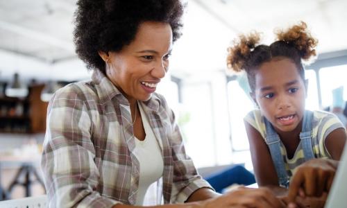 African American mother and daughter work on laptop together at home