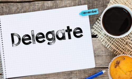 Notebook with delegate sign and sticker remember on wooden desk with cup of coffee and muffin