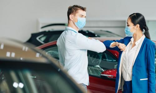 customer and car salesperson wearing masks bump elbows