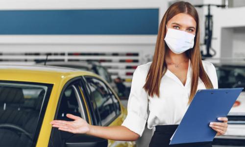 female car salesperson holding arm out by car