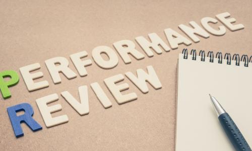 Performance review text with open spiral notebook and pen on brown background