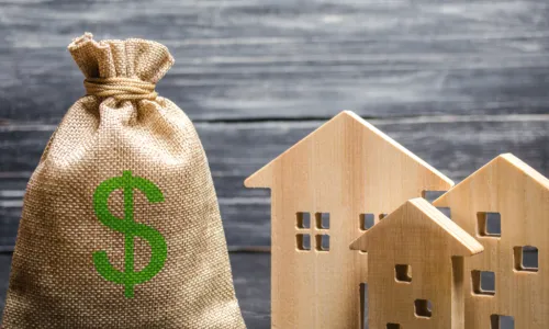 burlap bag with green dollar sign on it next to wooden houses