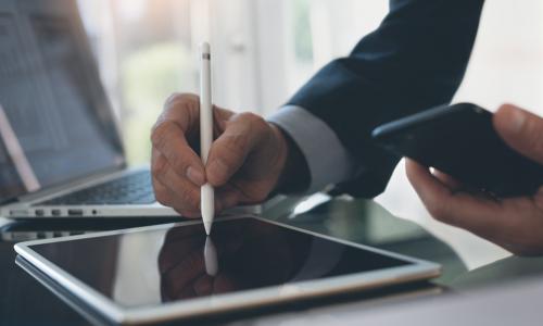 business man signing on tablet with laptop in background