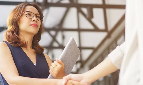 serious looking Asian businesswoman holding a portfolio shakes hands with vendor