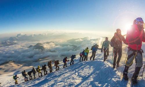 group of mountain climbers trekking up a snowy slope on a sunny day