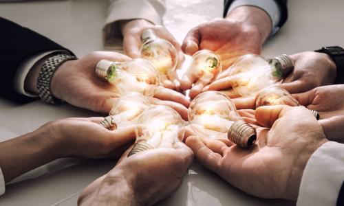 group of business people’s hands holding out glowing lightbulbs to represent team brainstorming and innovation