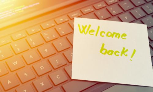 welcome back written on sticky note stuck to open laptop keyboard