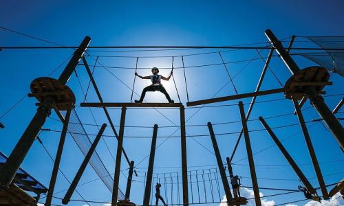 people climbing on a high ropes obstacle course with blue sky and fluffy clouds in the background