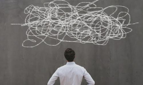 businessman studies squiggle of complexity drawn on chalkboard