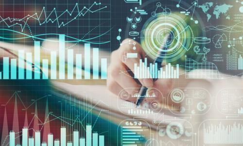 many digital financial graphs and charts displayed in front of hand taking notes in background