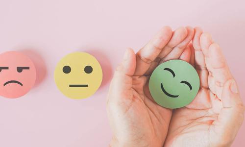 hands holding paper circle green smiley face next to red angry and yellow neutral faces
