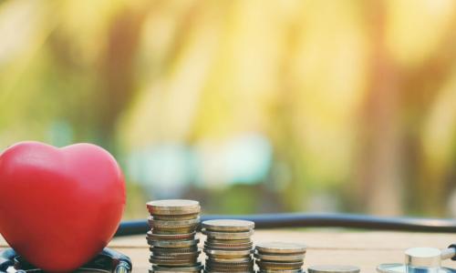 Red heart and stacks of coins surrounded by a stethoscope checking for financial wellness