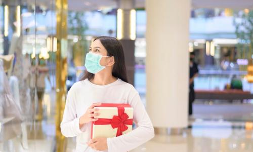 masked woman shopping in mall carrying present with red bow