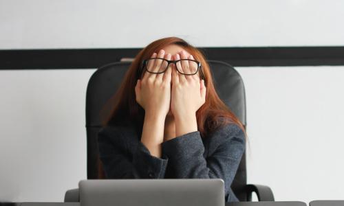 stressed business woman covering her eyes while sitting at desk feeling burnout