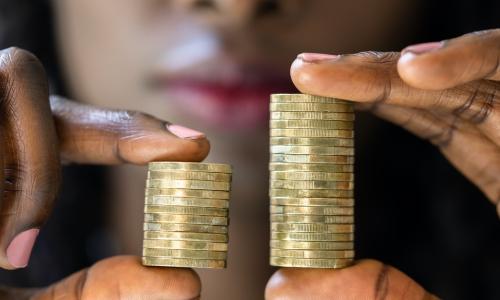 Black woman holds two stacks of coins where one is noticeably smaller